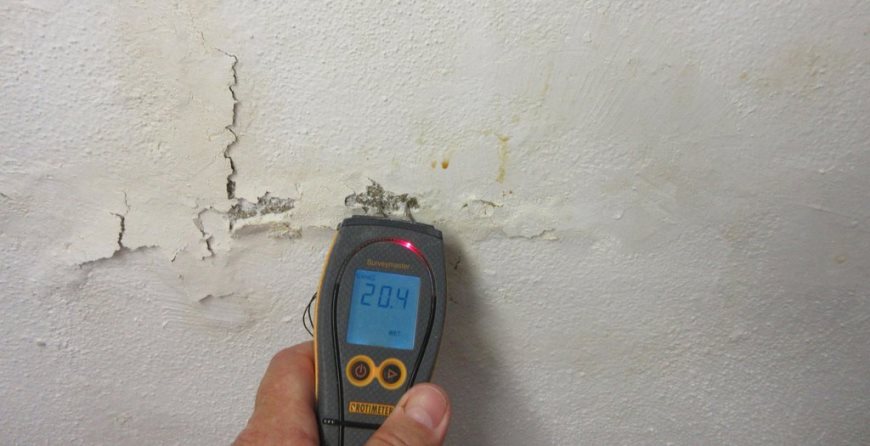 Close-up of a building inspector using a digital moisture meter to check wall dampness and cracks during a property defect inspection.