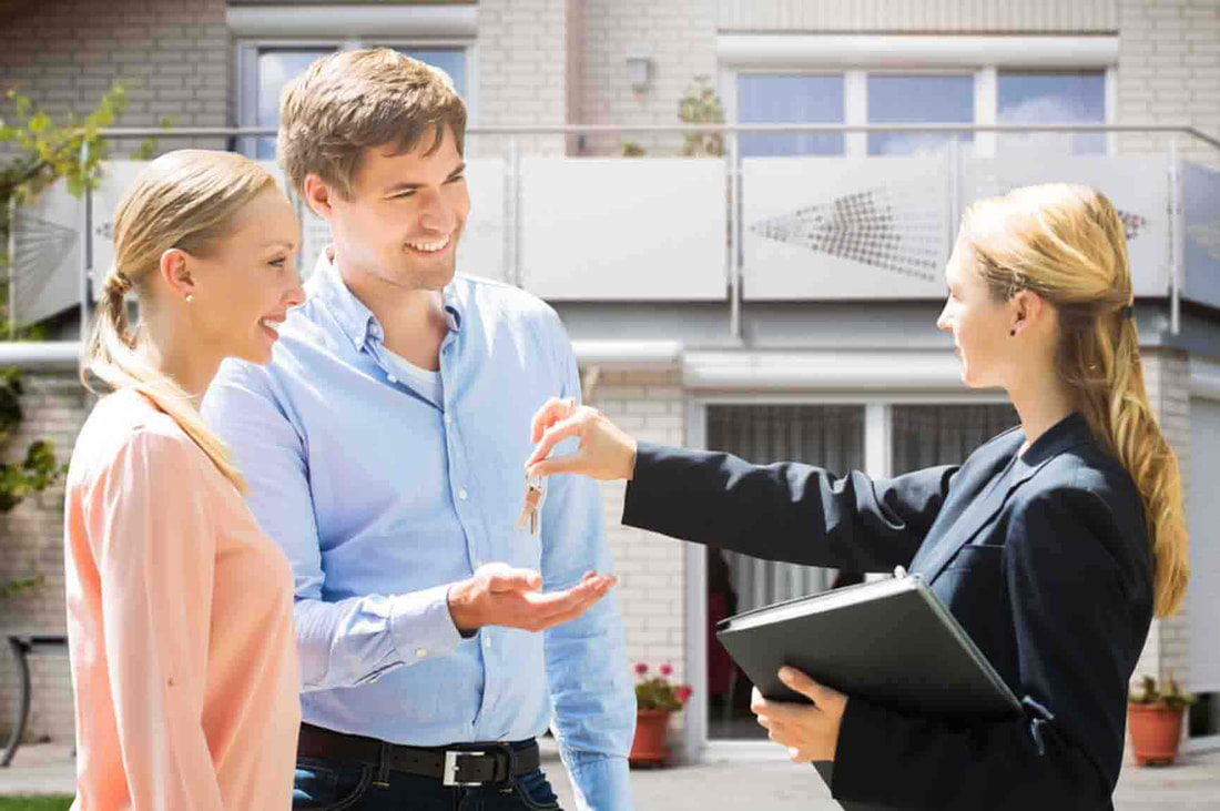 Couple receiving keys to a new property from a real estate professional outside the building